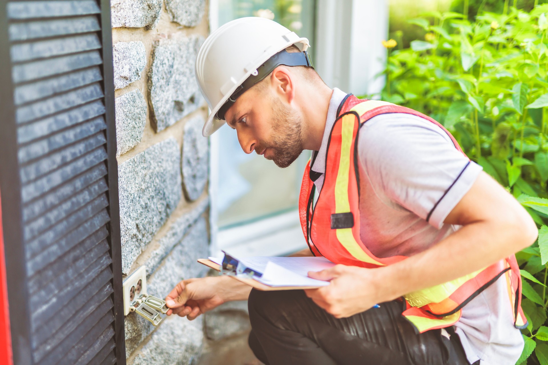 Man with a white hard hat holding a clipboard, inspect house